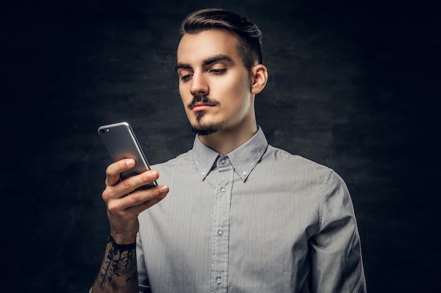 Foto gratuita retrato de estudio de un guapo hipster barbudo con un tatuaje en el brazo usando un smartphone.