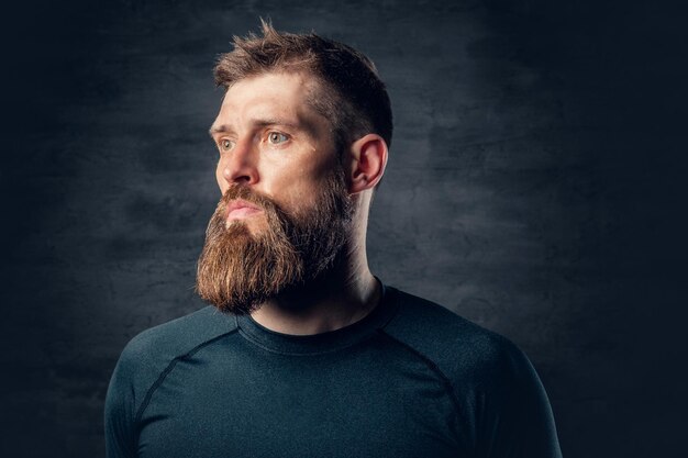 Retrato de estudio de un hombre barbudo deportivo vestido con ropa deportiva gris sobre fondo gris oscuro.