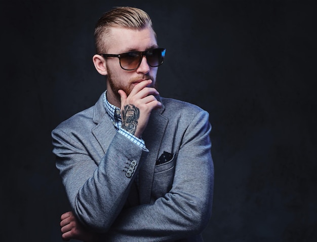 Foto gratuita retrato de estudio de hombre barbudo pelirrojo vestido con traje y gafas de sol sobre fondo gris.