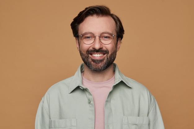 Foto gratuita retrato de estudio de un hombre barbudo posando sobre un fondo beige mirando a la cámara con una amplia sonrisa en la cara