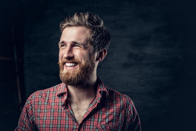 El retrato de estudio de un hombre barbudo rubio positivo vestido con una camisa de lana roja hace conversación.