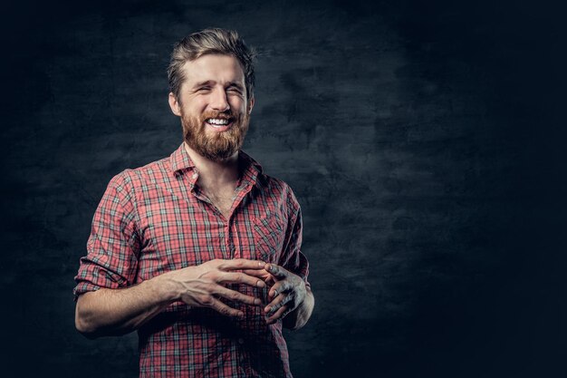 El retrato de estudio de un hombre barbudo rubio positivo vestido con una camisa de lana roja hace conversación.