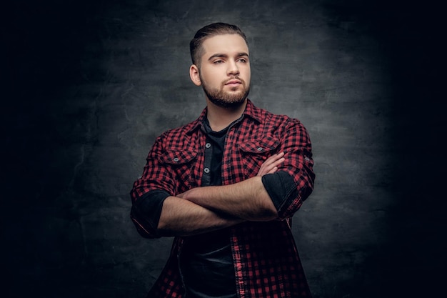 Retrato de estudio de hombre hipster barbudo con brazos cruzados, vestido con una camisa de lana roja sobre fondo gris.