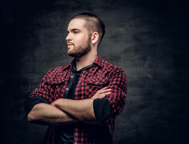 Retrato de estudio de hombre hipster barbudo con brazos cruzados, vestido con una camisa de lana roja sobre fondo gris.