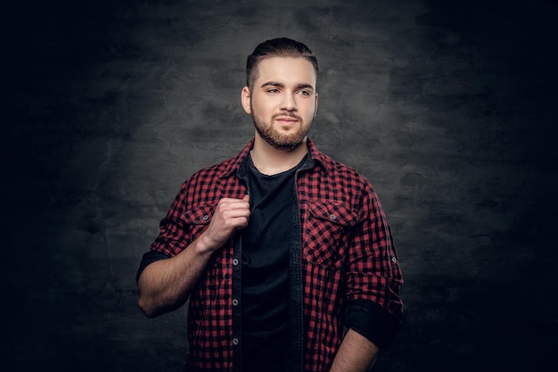 Retrato de estudio de un hombre hipster barbudo vestido con una camisa de lana roja sobre fondo gris.