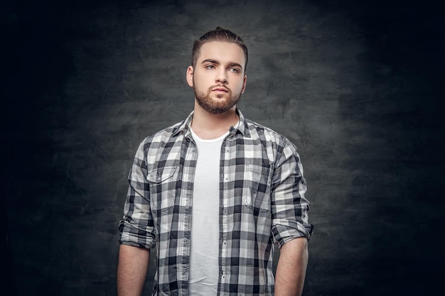 Retrato de estudio de un hombre hipster barbudo vestido con una camisa de lana sobre fondo gris.