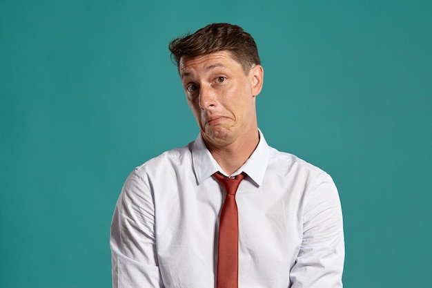 Foto gratuita retrato de estudio de un joven divertido con un clásico pantalones blanco y corbata roja que parece confundido mientras posa sobre un fondo azul. corte de pelo con estilo. concepto de emociones sinceras. copie el espacio.