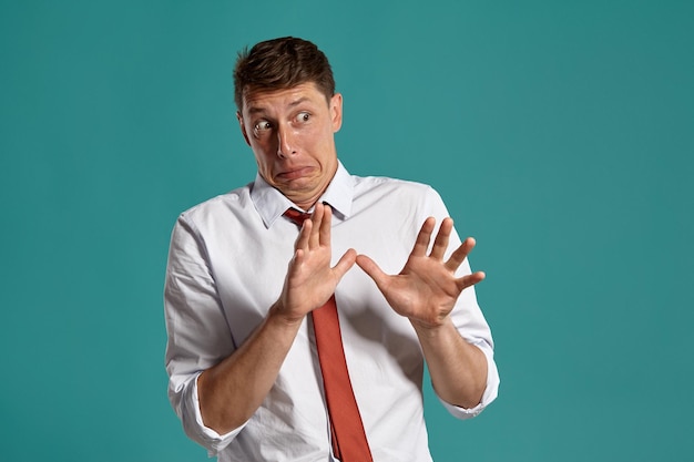 Retrato de estudio de un joven inteligente con un clásico pantalones blanco y corbata roja que parece haber visto algo repugnante mientras posa sobre un fondo azul. Corte de pelo con estilo. Concepto de emociones sinceras