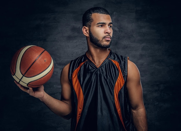 Retrato de estudio del jugador de baloncesto negro sostiene una pelota sobre fondo gris.