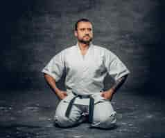 Foto gratuita retrato de estudio del luchador de karate brutal barbudo vestido con un kimono blanco sobre fondo gris.