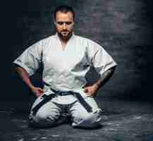 Foto gratuita retrato de estudio del luchador de karate brutal barbudo vestido con un kimono blanco sobre fondo gris.