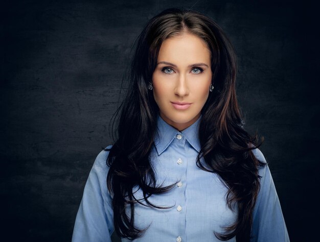 Retrato de estudio de mujer morena en una camisa azul sobre fondo gris.