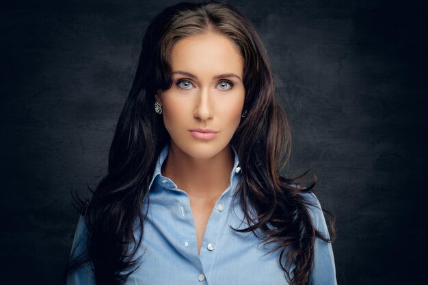 Retrato de estudio de mujer morena en una camisa azul sobre fondo gris.