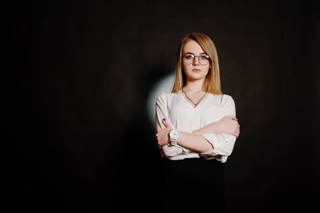 Retrato de estudio de mujer de negocios rubia en gafas blusa blanca y falda negra sobre fondo oscuro Concepto de mujer exitosa y chica elegante