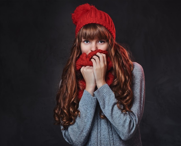 Retrato de estudio de mujer pelirroja con ropa de abrigo posando sobre fondo gris.