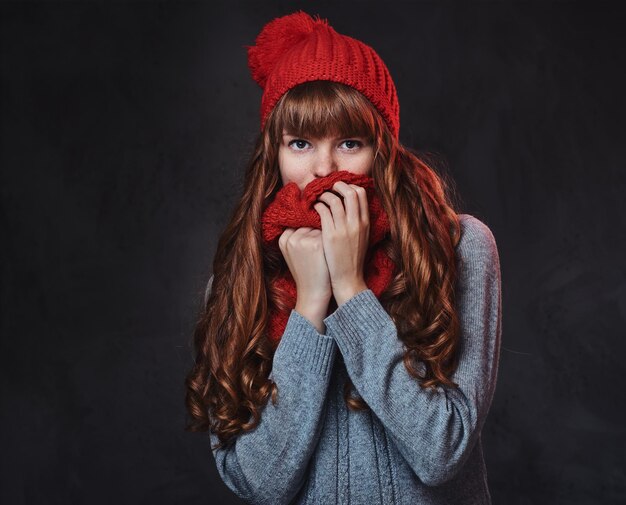 Retrato de estudio de mujer pelirroja con ropa de abrigo posando sobre fondo gris.