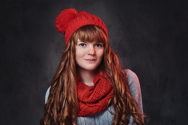 Retrato de estudio de mujer pelirroja con ropa de abrigo posando sobre fondo gris.