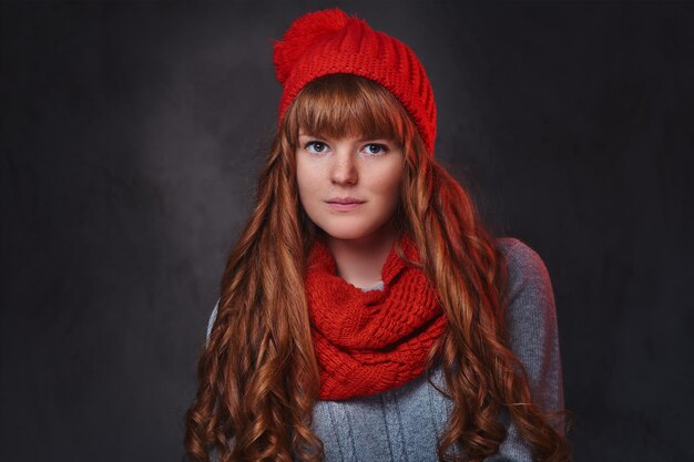 Retrato de estudio de mujer pelirroja con ropa de abrigo posando sobre fondo gris.