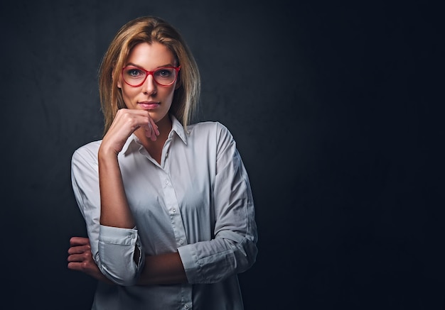 Retrato de estudio de mujer rubia vestida con una camisa blanca y anteojos rojos.