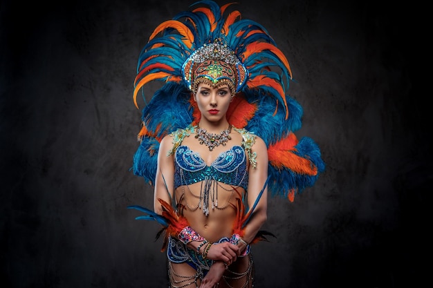 Retrato de estudio de una mujer sexy en un colorido y suntuoso traje de plumas de carnaval, posando sobre un fondo oscuro.