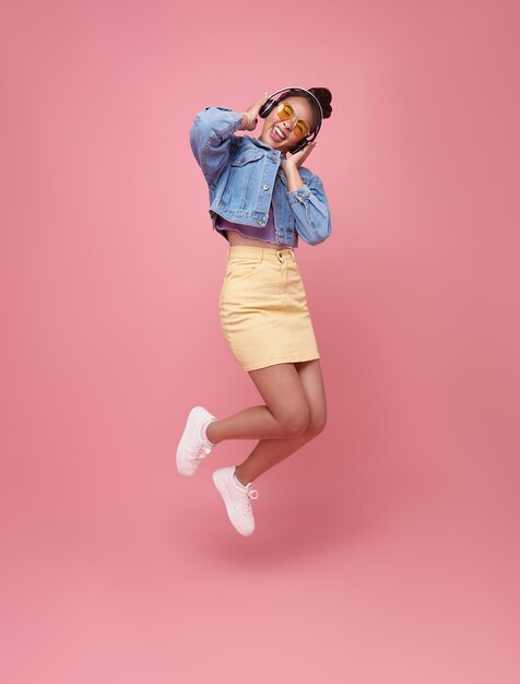 Retrato de estudio de salto de mujer asiática joven divertida escuchando música con auriculares bailando