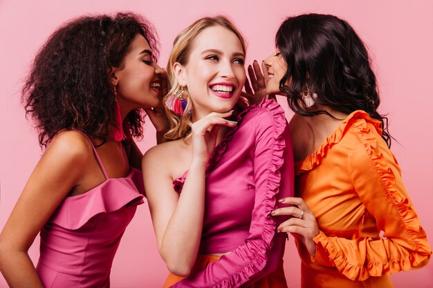 Retrato de estudio de tres amigos internacionales sonriendo sobre pared rosa