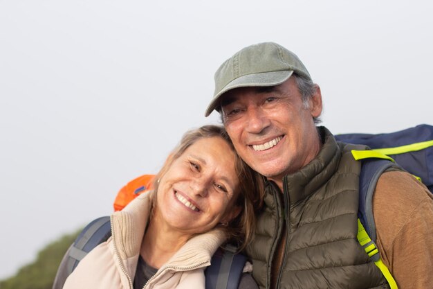 Retrato de excursionistas ancianos sonrientes. Hombre y mujer con mochilas mirando a la cámara, apoyándose en el hombro. Senderismo, concepto de familia