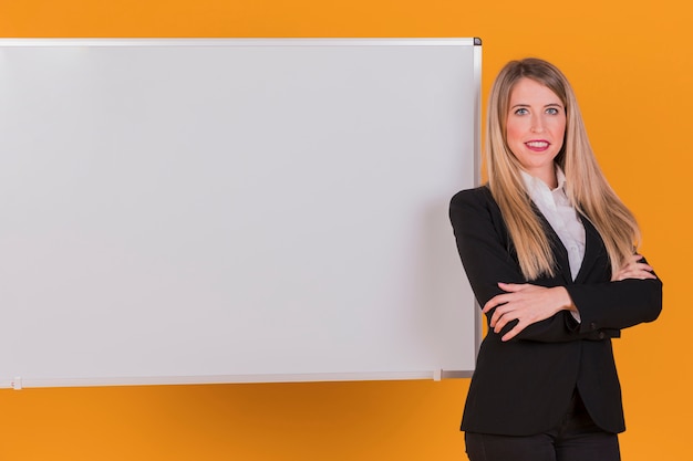 Foto gratuita retrato de una exitosa joven empresaria de pie cerca de la pizarra contra un fondo naranja