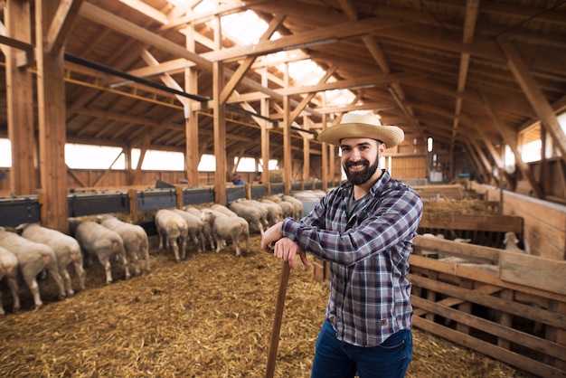 Foto gratuita retrato de exitoso agricultor ganadero de pie con orgullo en el establo de ovejas