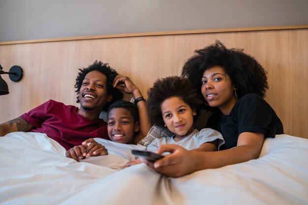 Retrato de familia afroamericana feliz viendo una película en la cama en el dormitorio en casa. Estilo de vida y concepto de familia.