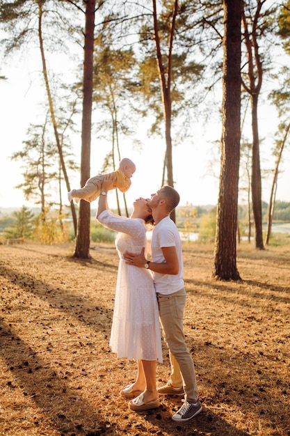 Retrato de familia atractiva joven con hijo pequeño, posando en el hermoso bosque de pinos de otoño en un día soleado. Hombre guapo y su bella esposa morena