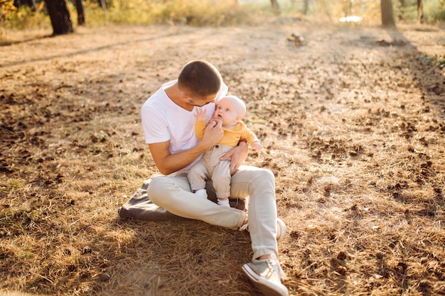 Retrato de familia atractiva joven con hijo pequeño, posando en el hermoso bosque de pinos de otoño en un día soleado. Hombre guapo y su bella esposa morena