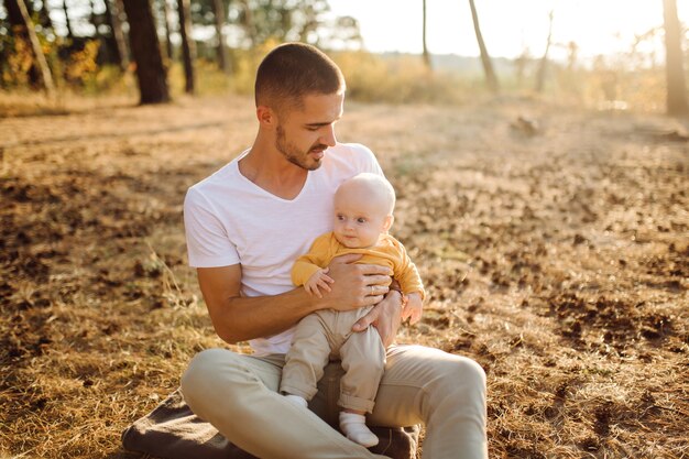 Retrato de familia atractiva joven con hijo pequeño, posando en el hermoso bosque de pinos de otoño en un día soleado. Hombre guapo y su bella esposa morena