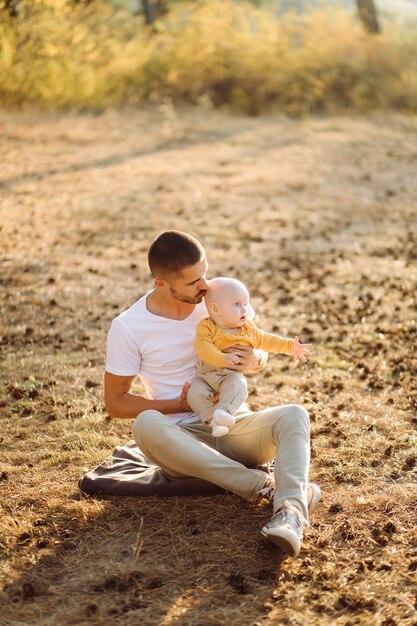 Retrato de familia atractiva joven con hijo pequeño, posando en el hermoso bosque de pinos de otoño en un día soleado. Hombre guapo y su bella esposa morena