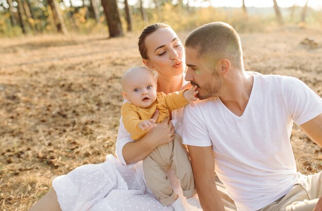 Retrato de familia atractiva joven con hijo pequeño, posando en el hermoso bosque de pinos de otoño en un día soleado. Hombre guapo y su bella esposa morena