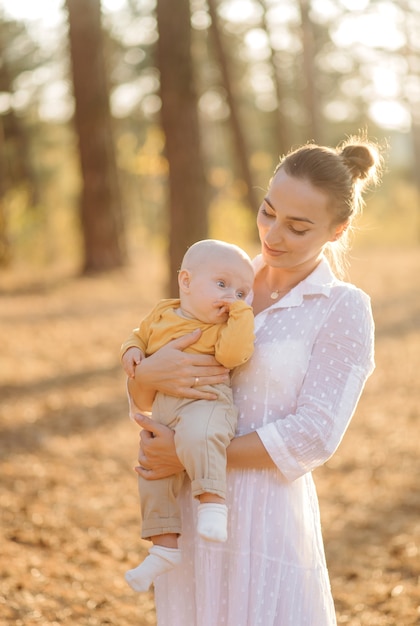 Retrato de familia atractiva joven con hijo pequeño, posando en el hermoso bosque de pinos de otoño en un día soleado. Hombre guapo y su bella esposa morena