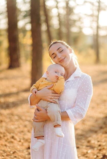 Retrato de familia atractiva joven con hijo pequeño, posando en el hermoso bosque de pinos de otoño en un día soleado. Hombre guapo y su bella esposa morena