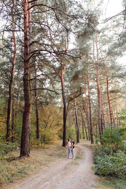 Retrato de familia atractiva joven con hijo pequeño, posando en el hermoso bosque de pinos de otoño en un día soleado. Hombre guapo y su bella esposa morena