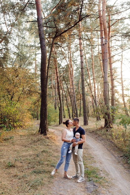 Retrato de familia atractiva joven con hijo pequeño, posando en el hermoso bosque de pinos de otoño en un día soleado. Hombre guapo y su bella esposa morena