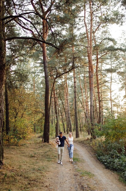 Retrato de familia atractiva joven con hijo pequeño, posando en el hermoso bosque de pinos de otoño en un día soleado. Hombre guapo y su bella esposa morena