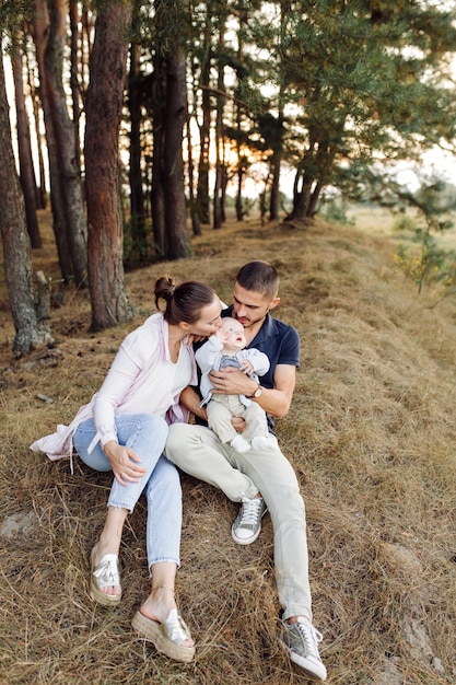 Retrato de familia atractiva joven con hijo pequeño, posando en el hermoso bosque de pinos de otoño en un día soleado. Hombre guapo y su bella esposa morena