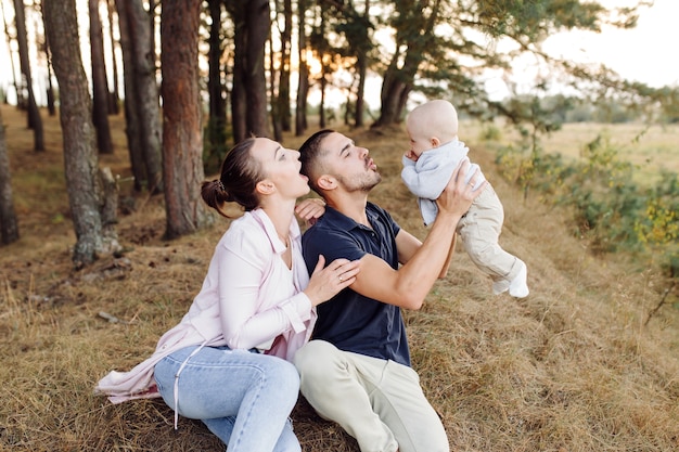 Retrato de familia atractiva joven con hijo pequeño, posando en el hermoso bosque de pinos de otoño en un día soleado. Hombre guapo y su bella esposa morena