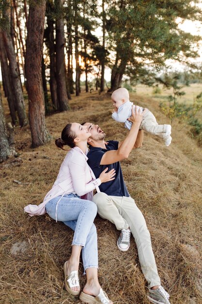 Retrato de familia atractiva joven con hijo pequeño, posando en el hermoso bosque de pinos de otoño en un día soleado. Hombre guapo y su bella esposa morena