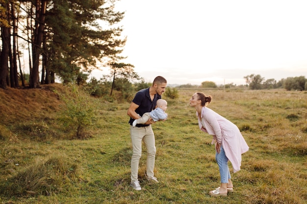 Retrato de familia atractiva joven con hijo pequeño, posando en el hermoso bosque de pinos de otoño en un día soleado. Hombre guapo y su bella esposa morena