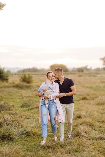 Retrato de familia atractiva joven con hijo pequeño, posando en el hermoso bosque de pinos de otoño en un día soleado. Hombre guapo y su bella esposa morena