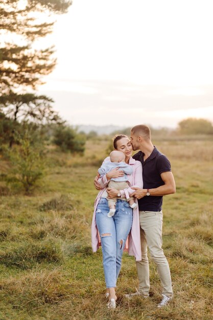 Retrato de familia atractiva joven con hijo pequeño, posando en el hermoso bosque de pinos de otoño en un día soleado. Hombre guapo y su bella esposa morena