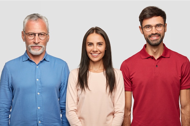 Foto gratuita retrato de familia de hombre maduro de pelo gris y su atractivo hijo, hija, parados de cerca, posar para fotos de álbumes, tener expresiones alegres, buenas relaciones. concepto de personas, edad y familia