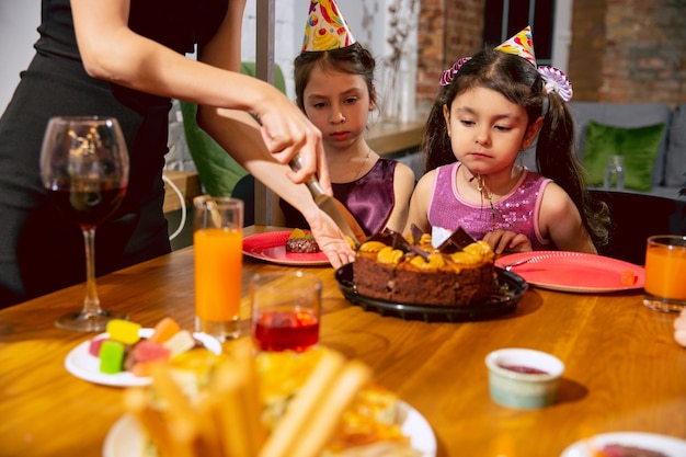 Retrato de familia multiétnica feliz celebrando un cumpleaños en casa. Gran familia comiendo pastel y bebiendo vino mientras saluda y se divierte a los niños. Celebración, familia, fiesta, concepto de hogar.