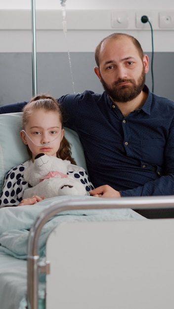 Retrato de familia triste mirando a la cámara mientras sostiene las manos de la hija enferma