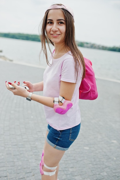 Retrato de una fantástica joven patinando con su teléfono en las manos en el parque al lado del lago